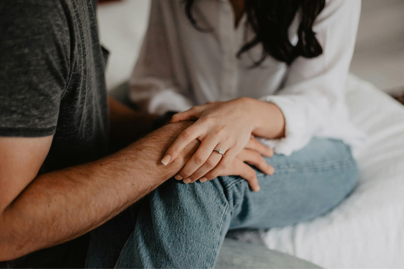 A couple sits closely together. The woman, wearing a white blouse, gently places her hand with an engagement ring over the man's arm. The man is dressed in a gray shirt and blue jeans. Amidst their cozy and intimate setting, they discuss the latest VESSA amendments impacting employee leave compliance.