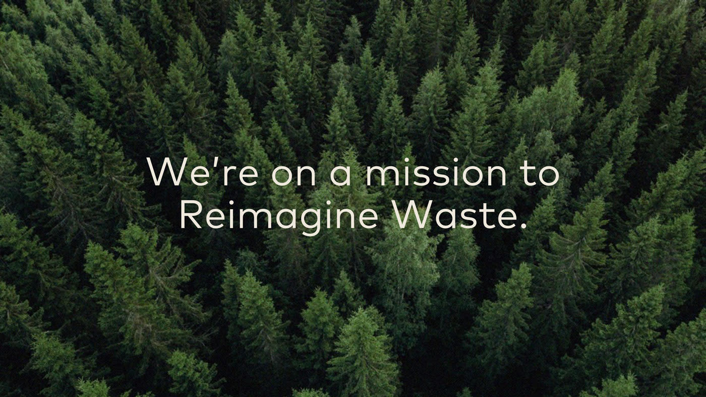 Aerial view of a dense forest of green pine trees with the text "We're on a mission to Reimagine Waste" overlaid in the center, highlighting our sustainability initiatives.